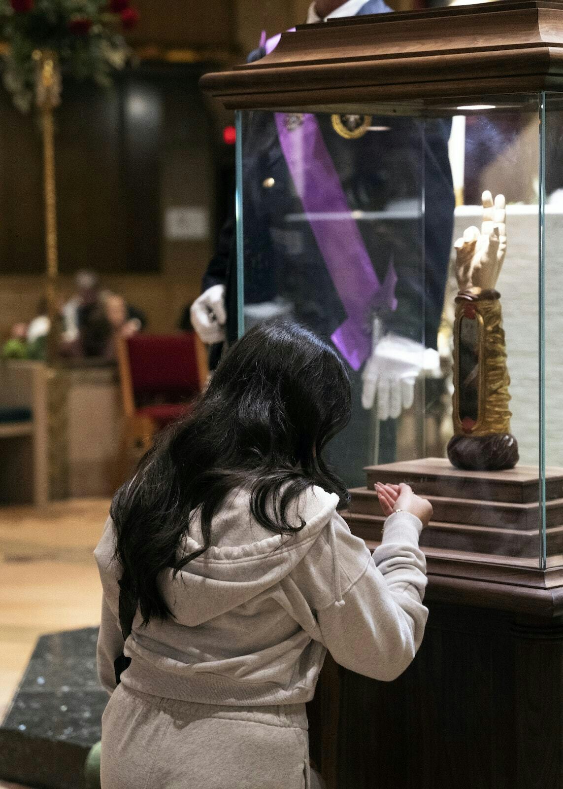 Una mujer se arrodilla en oración ante la reliquia de San Judas, que se encuentra en un gran relicario que simula el brazo derecho del santo, levantado en señal de bendición.