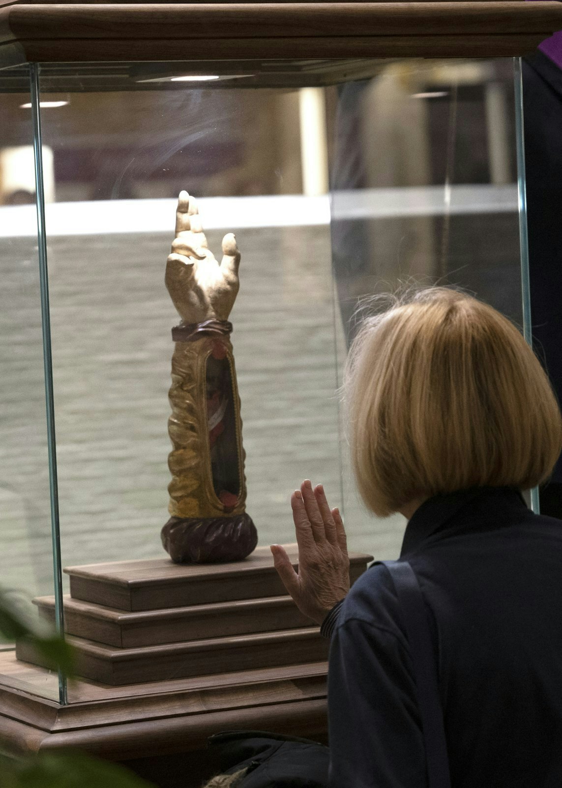 Una mujer apoya su mano en el cristal mientras reza un instante con el "Apóstol de lo Imposible".