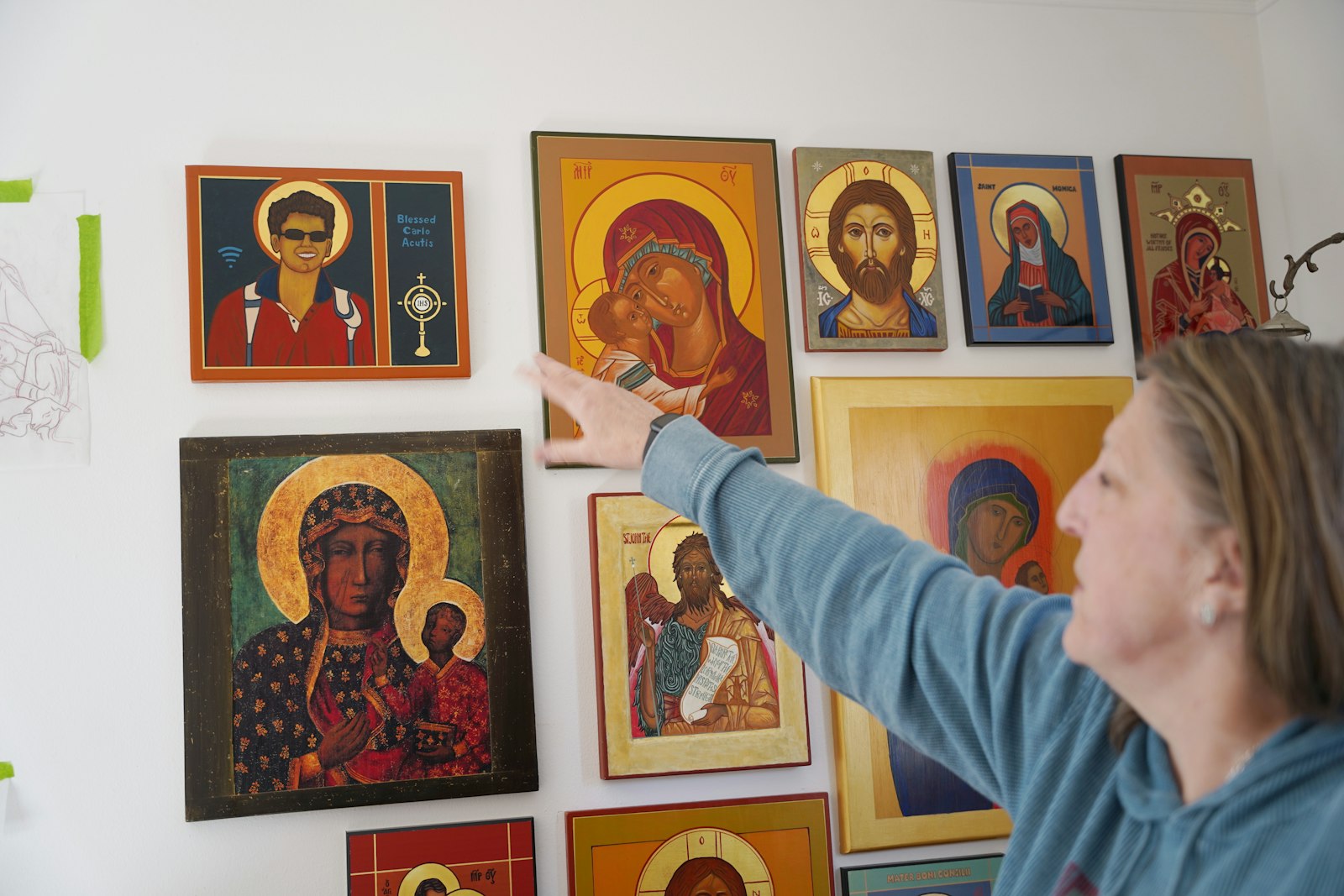 Crombie displays samples of her work in her home office, including one of Blessed Carlo Acutis, with Carlo depicted as wearing sunglasses and the WiFi symbol to the left of the icon.