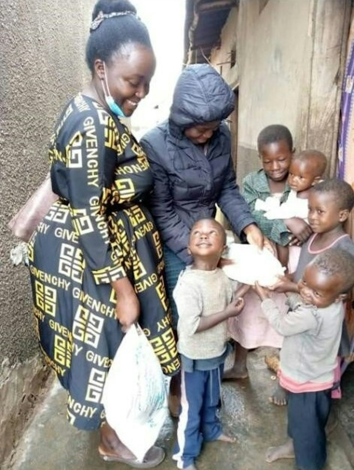 Ida Nakalembe, a la izquierda, y Ruth Lunkuse, de Ria Child Care & Women Empowerment Ministries, entregan ropa y material escolar a Marvin Lubowa, de primer grado (mirando hacia arriba), y a otros niños. (Cortesía de Joseph Kirembwe)