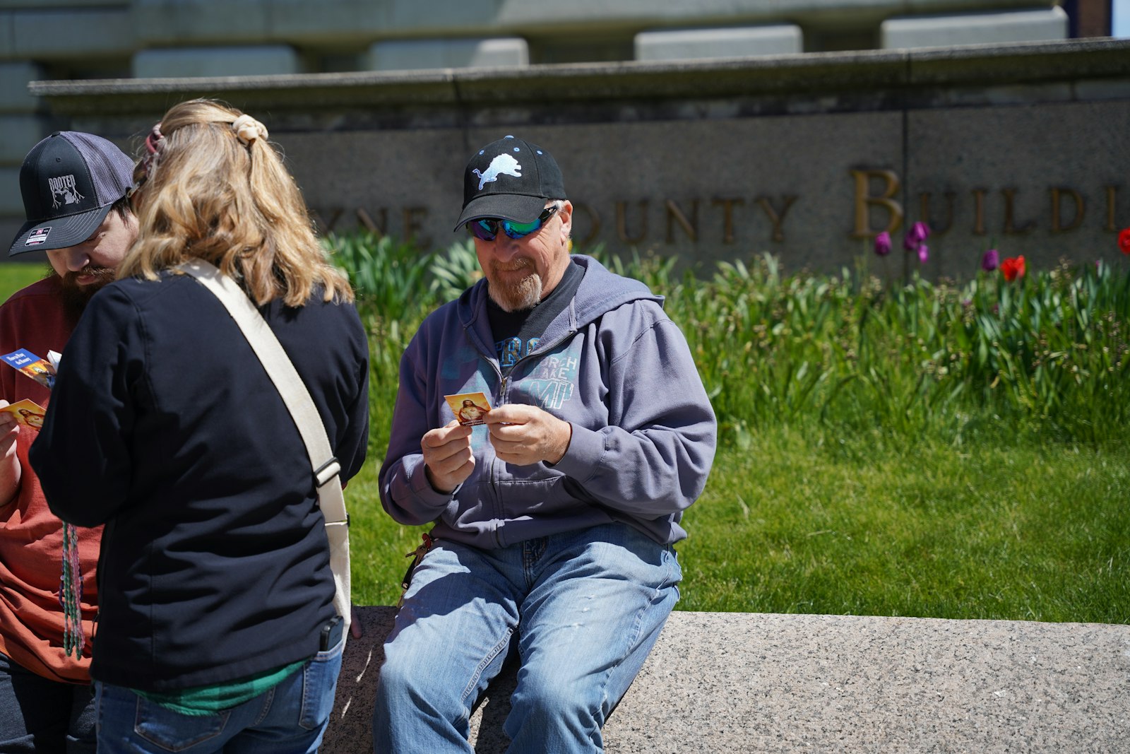 Beth Schuele of St. Paul Street Evangelization hands a prayer card to a Detroit Lions fan sitting in front of the old Wayne County Building on draft day.