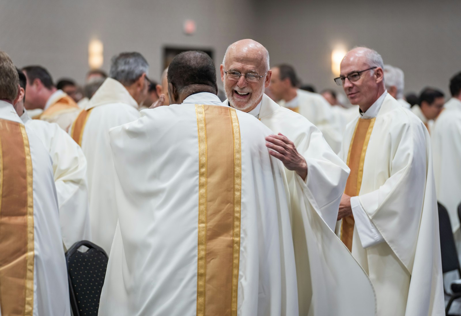 Priests of the Archdiocese of Detroit greet one another with hugs and smiles during a Mass on June 28, the second day of the Missionary Renewal Assembly at the Suburban Collection Showplace in Novi.