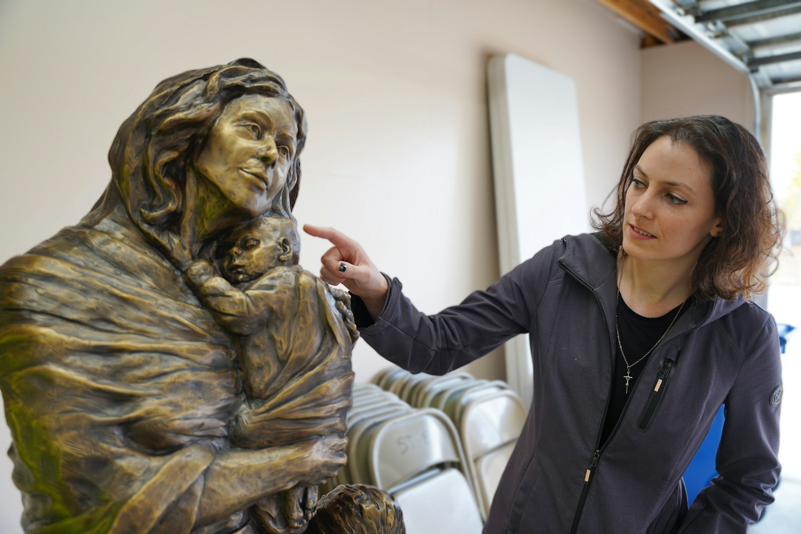 Artist Mary Dudek points out a detail on the statue of the Blessed Mother, depicted cradling an infant in her arms. (Daniel Meloy | Detroit Catholic)
