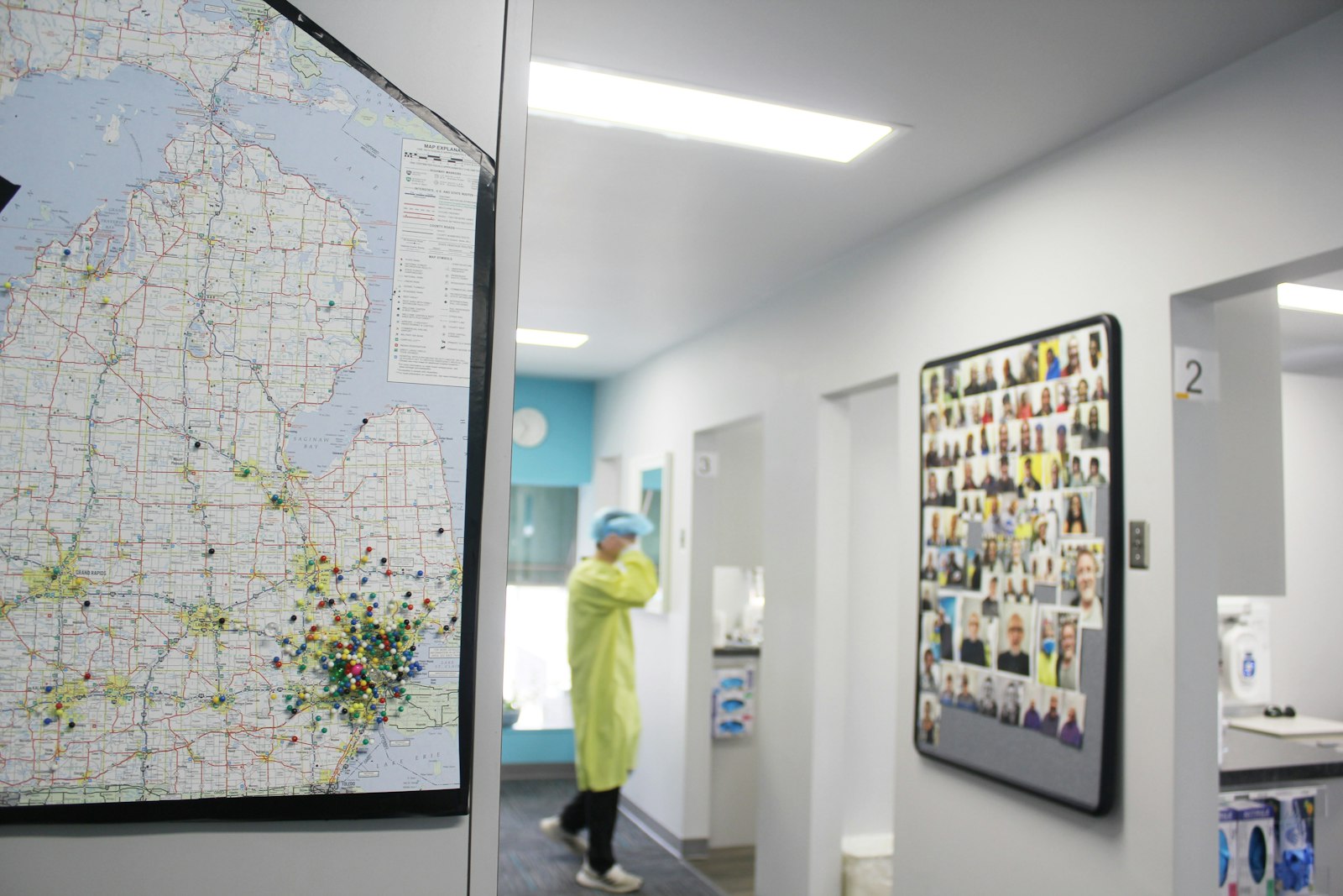 A la izquierda, un mapa con alfileres muestra los lugares de donde provienen los voluntarios de la Clínica Médica y Dental de Malta, mientras que un tablón de anuncios a la derecha muestra los rostros de los pacientes.