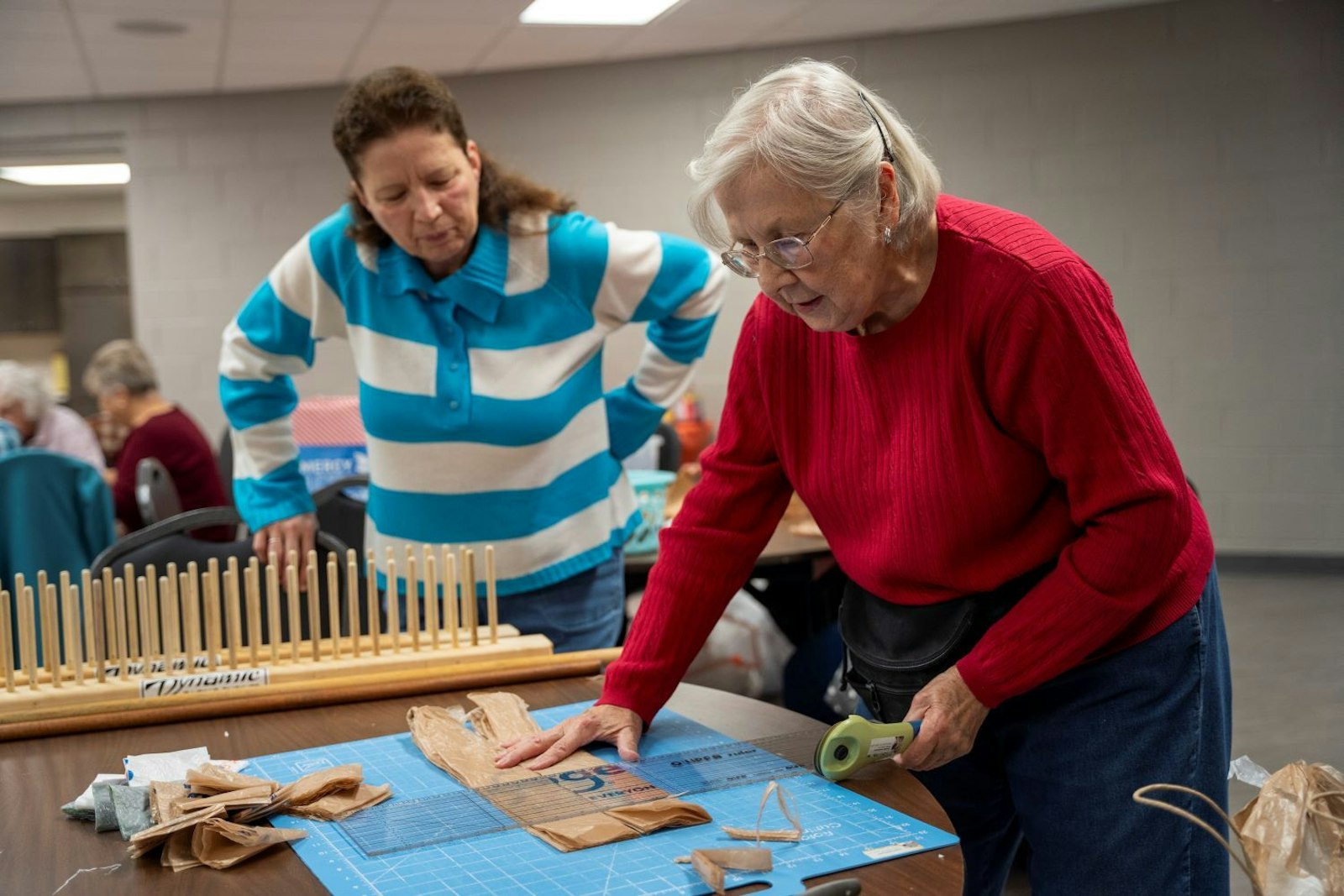 Dorothy Szulszewski prepares to cut a plastic shopping bag into small strands that will be turned into plastic yarn, which then will be woven into sleep mats, as Gloria Rouhib looks on.