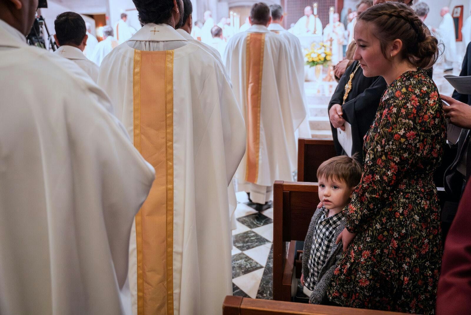 Un niño observa cómo un grupo de decenas de sacerdotes, obispos y diáconos caminan en procesión hacia la Cathedral of the Most Blessed Sacrament para la liturgia de inauguración del Obispo Monforton.