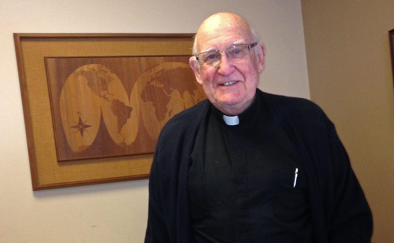 Msgr. Moloney is pictured next to a globe map in this 2015 file photo. Msgr. Moloney's personal touch and missionary heart made him specially suited to serve the missions, a roll he embraced for more than half a century in addition to his parish pastoral work. (Tim Keenan | Detroit Catholic file photo)