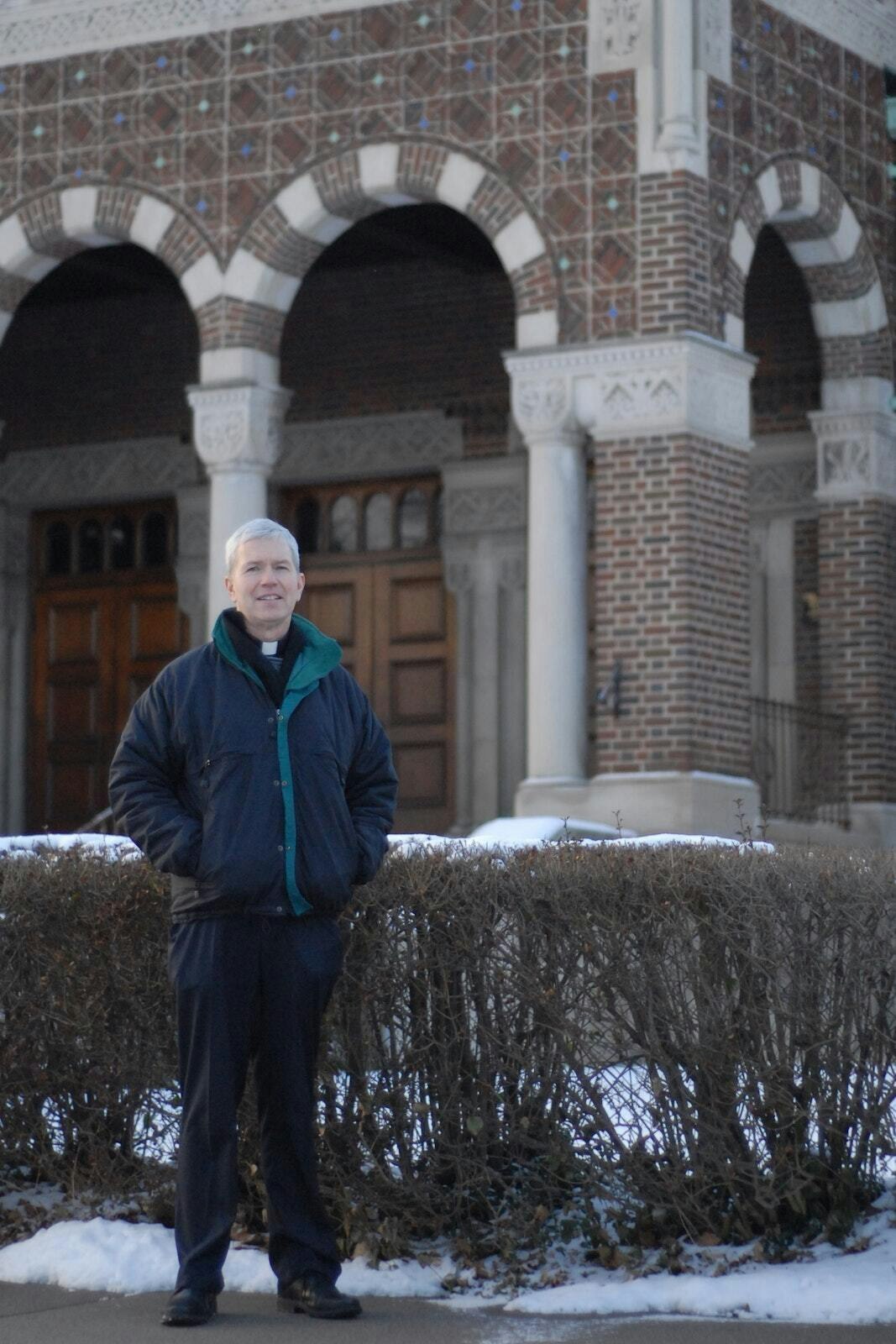 Msgr. Trapp stands in front of St. Augustine and St. Monica Parish on Detroit's east side in 2016. Under Msgr. Trapp's leadership, the parish organized a neighborhood association once a month to help residents build a sense of community and connection with the parish, as well as provide a host of services to those in need. (Michael Stechschulte | Detroit Catholic)