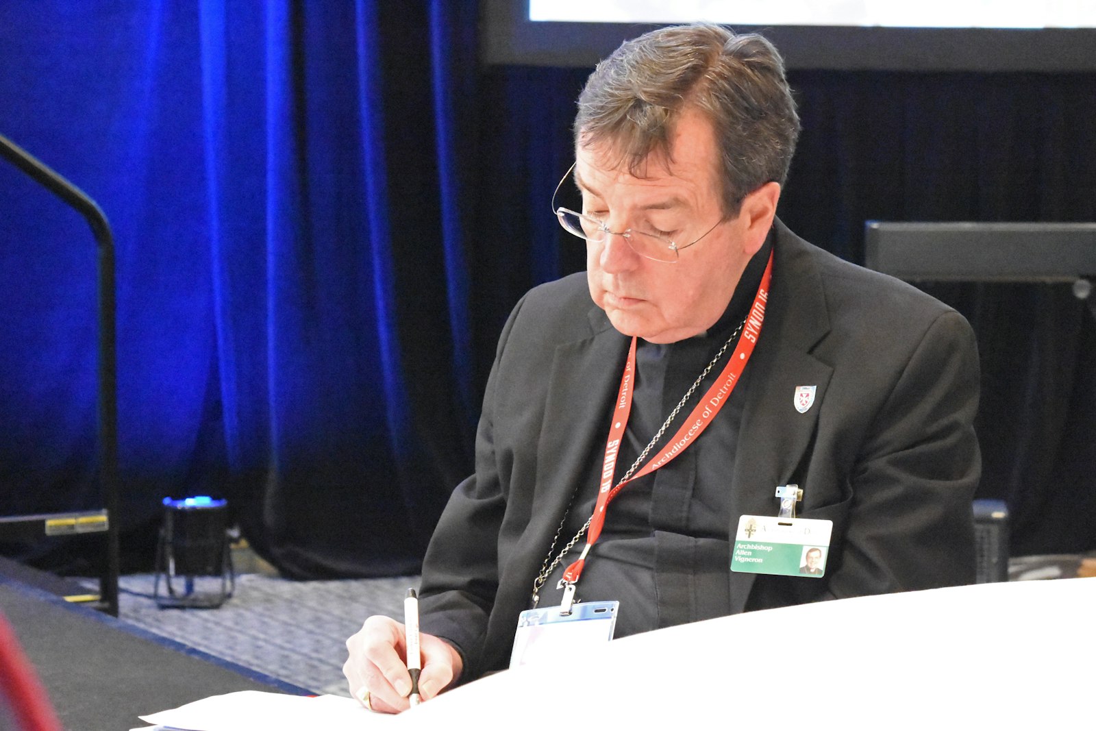 Archbishop Allen H. Vigneron takes notes while sitting a table during a session of Synod 16. (Michael Stechschulte | Detroit Catholic)