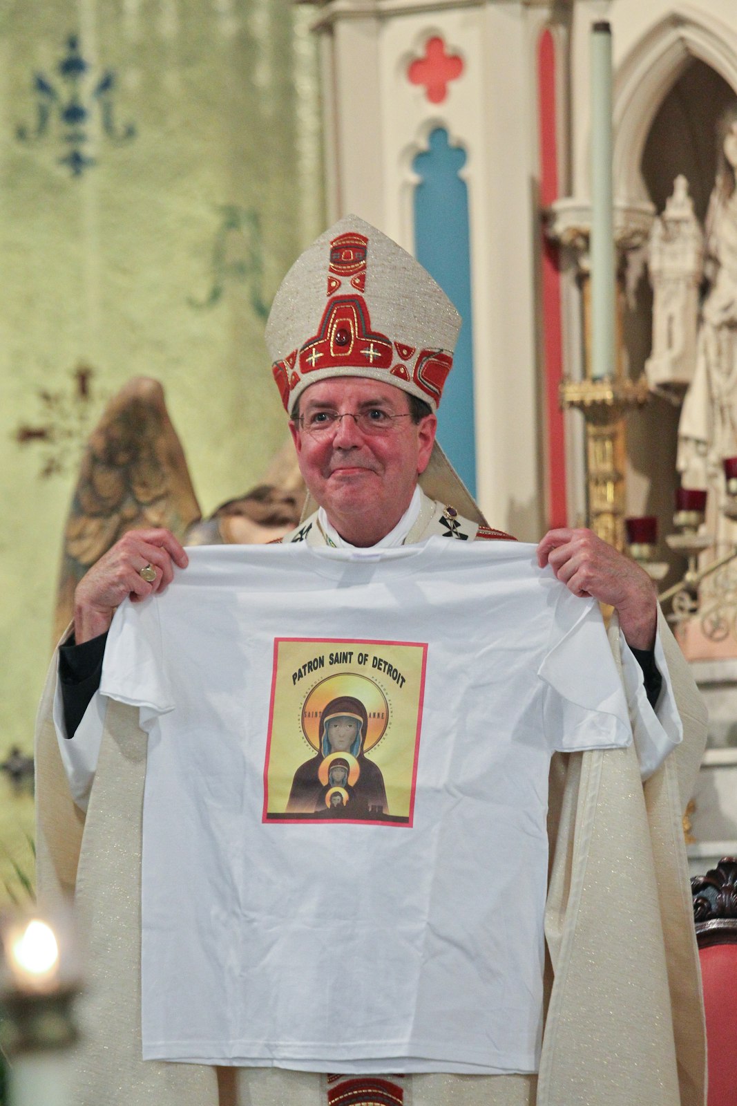 Archbishop Vigneron holds a t-shirt given to him as a gift in celebration of Ste. Anne being named the patroness of the Archdiocese of Detroit in 2011. (Joe Kohn | Detroit Catholic file photo)