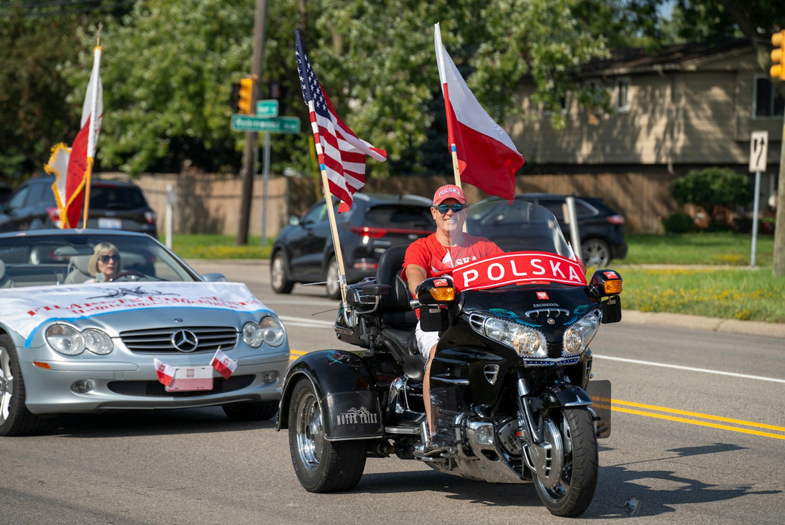 A man riding a motorcycle sporting Polish and American flags makes his way down Common Road.