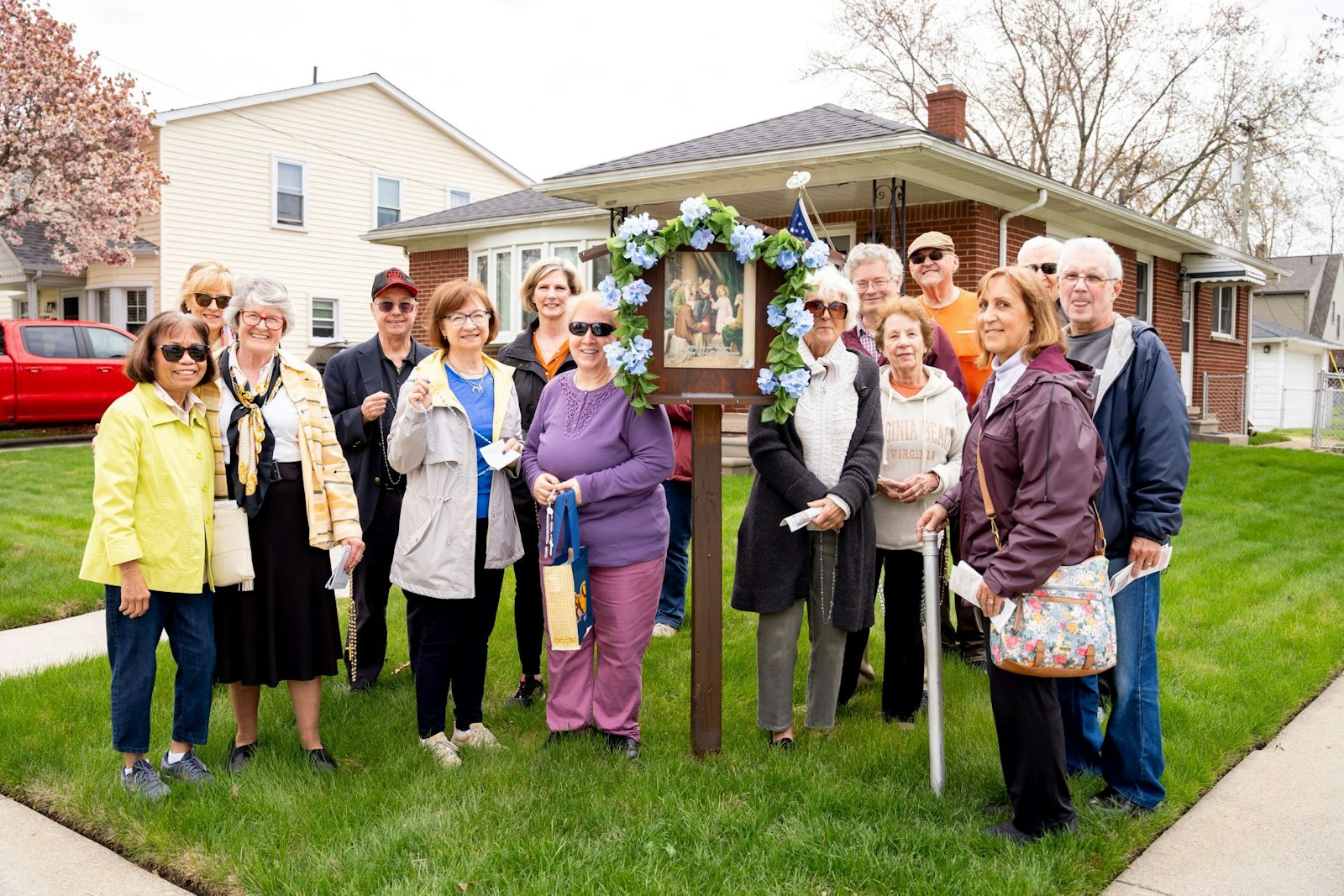 A group of Our Lady of the Scapular parishioners poses in front of one of the "rosary box" stations hosted in a parishioner's front yard along the pilgrimage route. The group is making weekly rosary pilgrimages throughout May.