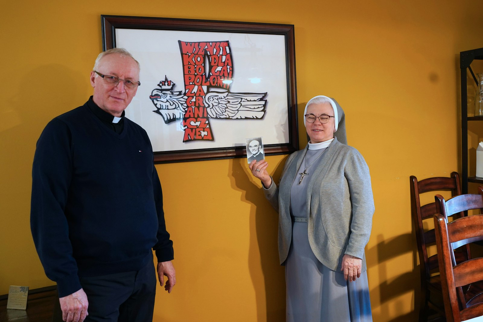 Fr. Jan Michalski, SChr., and Sr. Jodwiga Kokolus, MChr., stand next to a photo of the logo of the Society of Christ in the rectory of Our Lady of Czestochowa Parish.