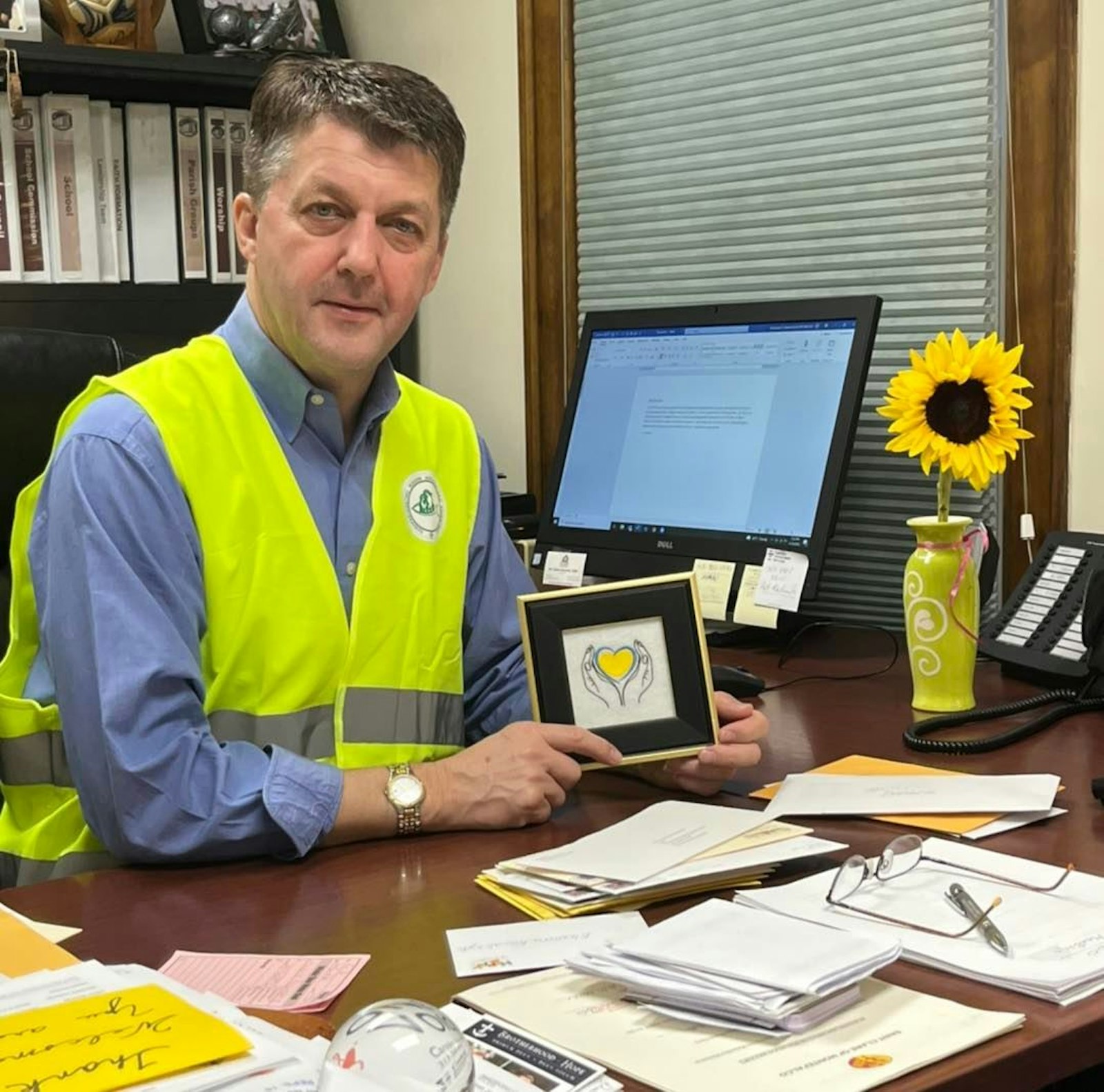 El padre Andrew Kowalczyk, CSMA, párroco de la parroquia de Santa Clara de Montefalco, sostiene una pequeña imagen enmarcada de un corazón azul y amarillo, los colores nacionales de Ucrania, abrazado por un par de manos. El P. Kowalczyk, que es de Polonia, dijo que su patria está mostrando el amor de Cristo en acción en su tratamiento de casi 3 millones de personas que huyen de la violencia en Ucrania.