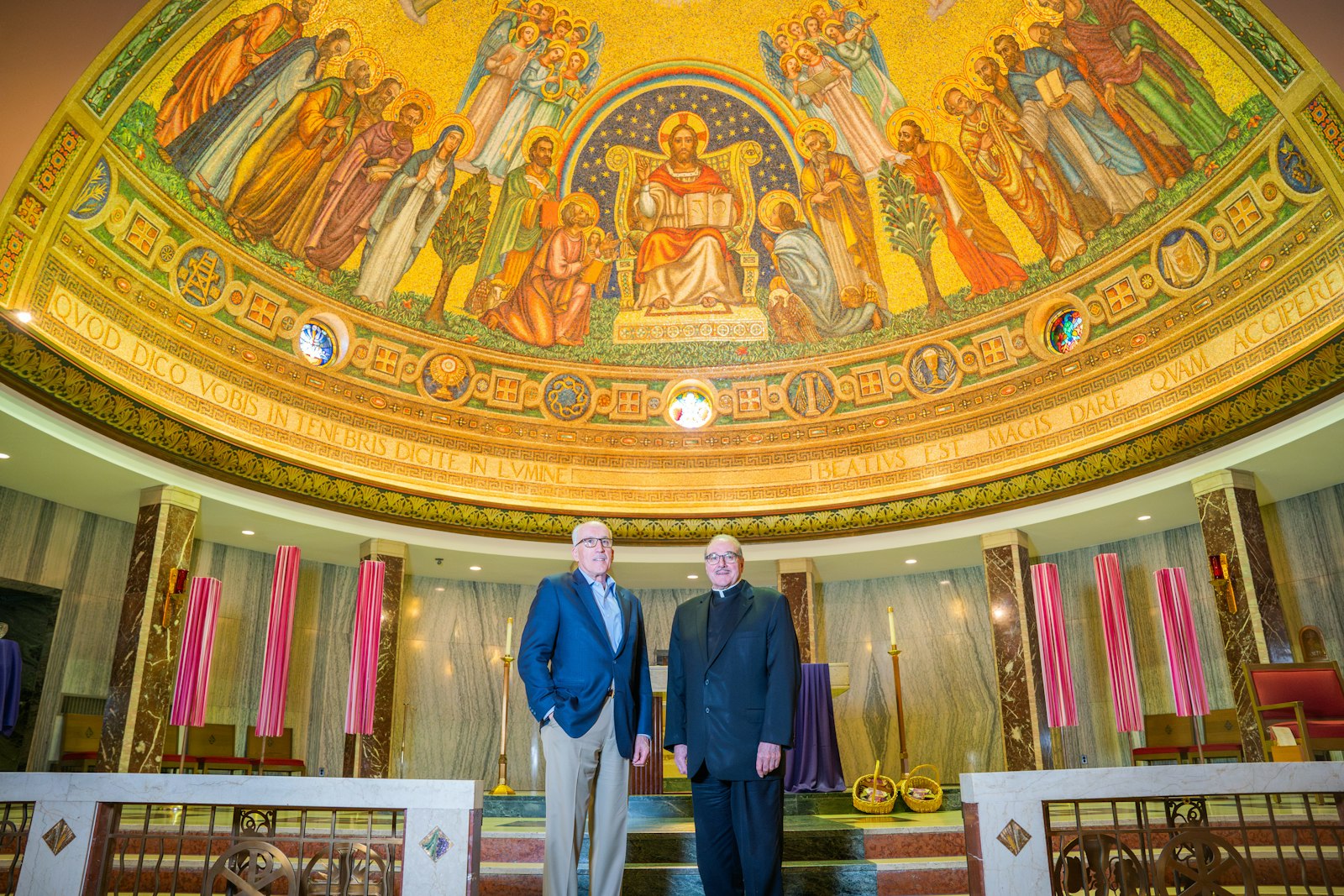 David Smydra, a St. Matthew parishioner, stands with Fr. Duane Novelly before the mosaic that overlooks the church's sanctuary. Smydra worked with Fr. Novelly on completing all the paperwork and procedures necessary to get St. Matthew Parish on the National Register of Historic Places. The two are standing beneath a mosaic crafted by Andrew Maglia. The 1,300-square foot mosaic was especially impressive to the team from the U.S. Department of the Interior that inspected St. Matthew Church during the historic designation process.