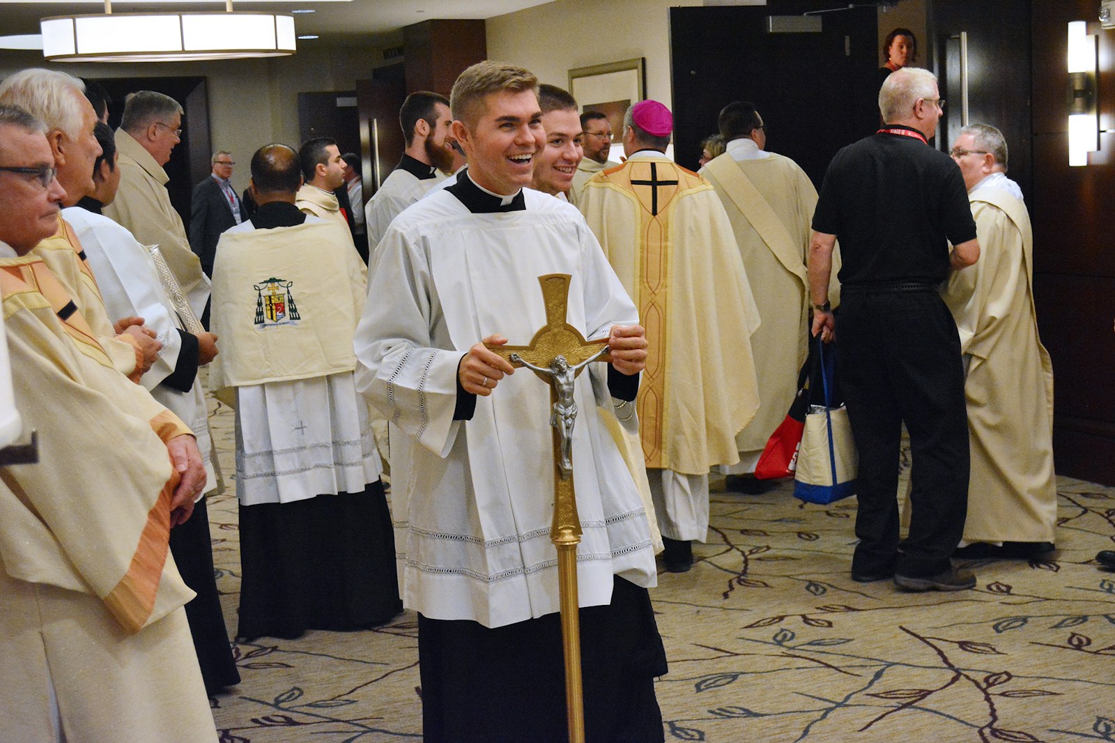 Seminarian Adam Nowak, now Fr. Adam Nowak, smiles as he holds the crucifix used in the opening procession of Synod 16 as clergy and laity gather for the opening session inside the Westin Book Cadillac hotel on Nov. 18, 2016. (Michael Stechschulte | Detroit Catholic)