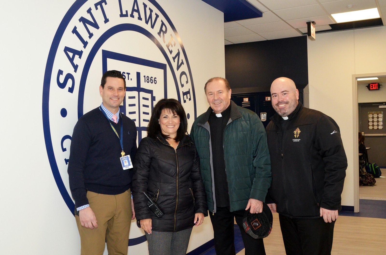 Brian Barker, subdirector, Lisa DiMercurio, directora, el P. Roman Pasieczny, párroco, y el P. Paul Graney, párroco asociado, posan delante del escudo de la Escuela Primaria St. Lawrence en el primer día de la inauguración oficial de la nueva escuela de educación media el 28 de febrero.