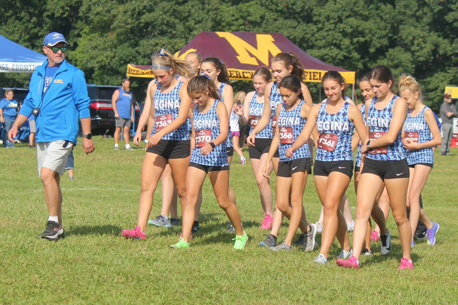 Veteran coach Gregg Golden leads his Warren Regina team to the starting line shortly before the start of the race at Hess-Hathaway Park in Waterford Township on Sept. 13. Senior Kennedy Roskopp said the Saddlelites’ main goal this season is to qualify for the state finals and improve their standing from 2022.