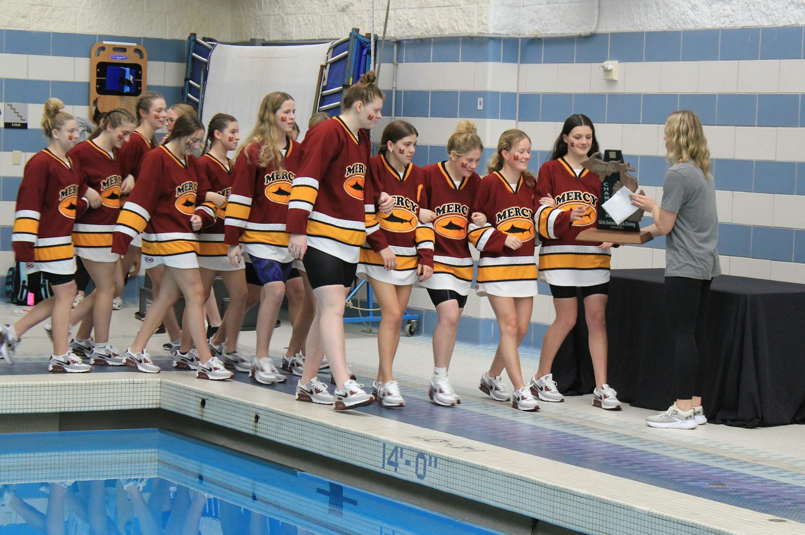 Farmington Hills Mercy swimmers accept the MHSAA Division 2 state championship trophy following the meet at Oakland University on Nov. 23. It was Mercy’s third consecutive state title and 13th overall.