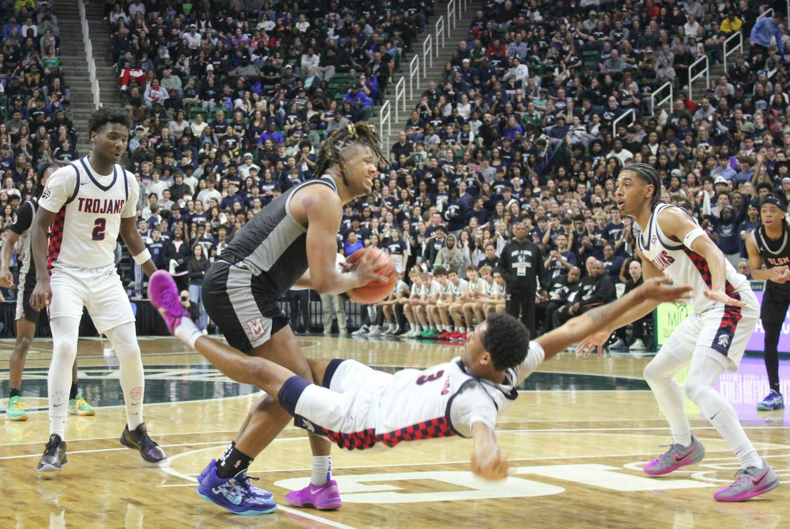 East Lansing’s Jayce Branson goes flying backward as he tries to stop Orchard Lake St. Mary’s senior Trey McKenney from launching a shot.